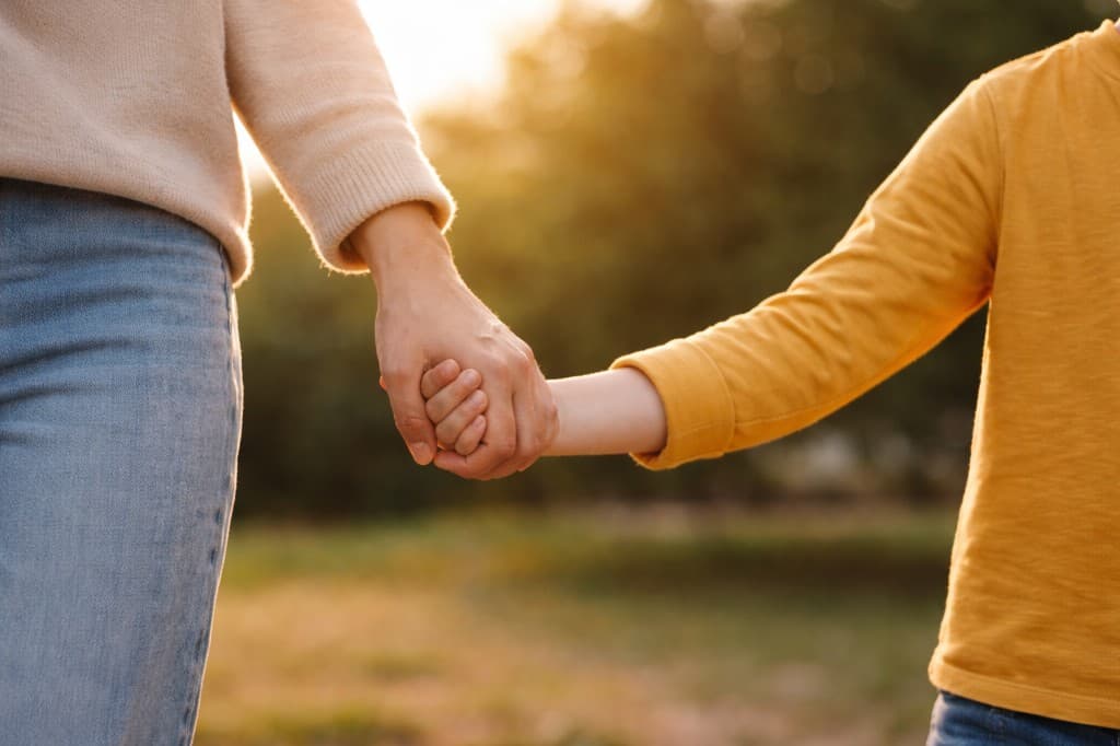 A parent and child holding hands while walking together outdoors in warm sunlight
